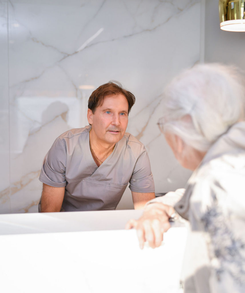 Tannhelsepersonell i samtale med pasient ved resepsjonen hos Drammen Tannlegesenter, i moderne og innbydende klinikkmiljø.